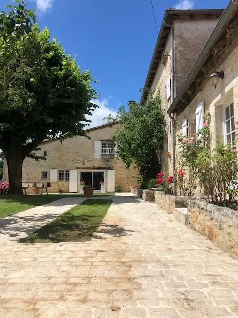 Façade en pierre et entrée du Clos Lagrange à Varaignes, allée pavée et grand arbre